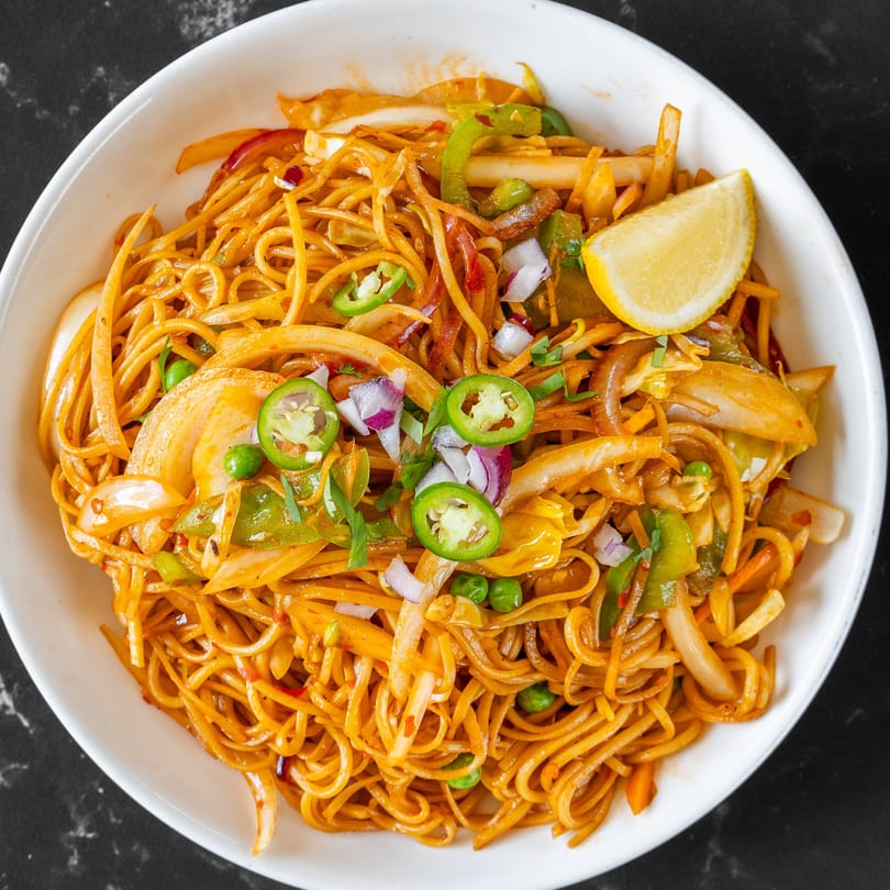 Swad Indian Restaurant's chili garlic noodles with vegetables, jalapeños, and a lemon wedge.