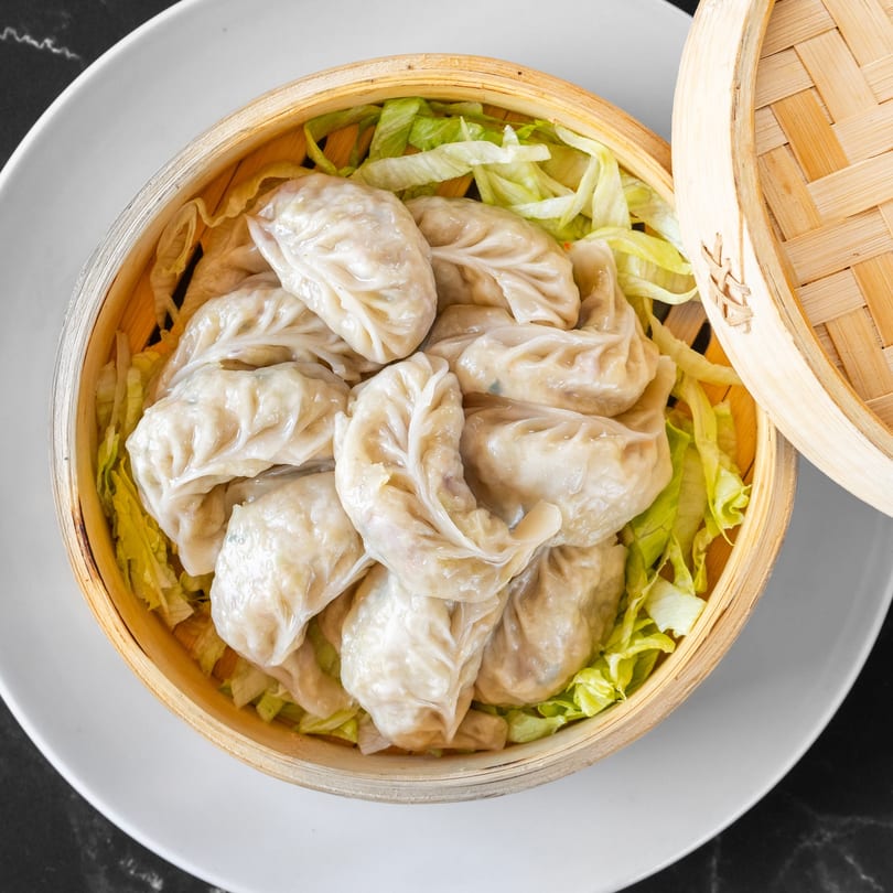 Steamed momos, an Indian dumpling, served in a bamboo steamer basket with lettuce at Swad Indian Restaurant.