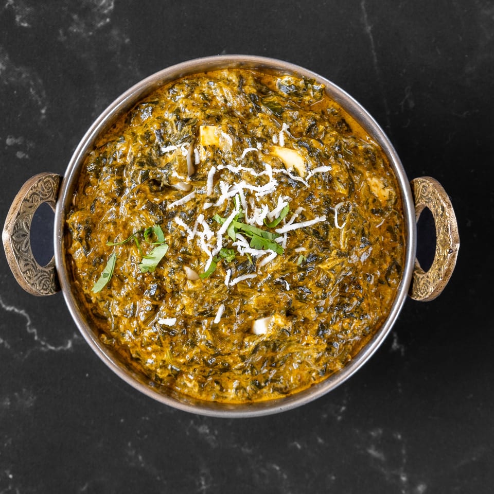 Palak Paneer, a vibrant green Indian spinach and cheese curry, garnished with fresh cilantro and shredded cheese.