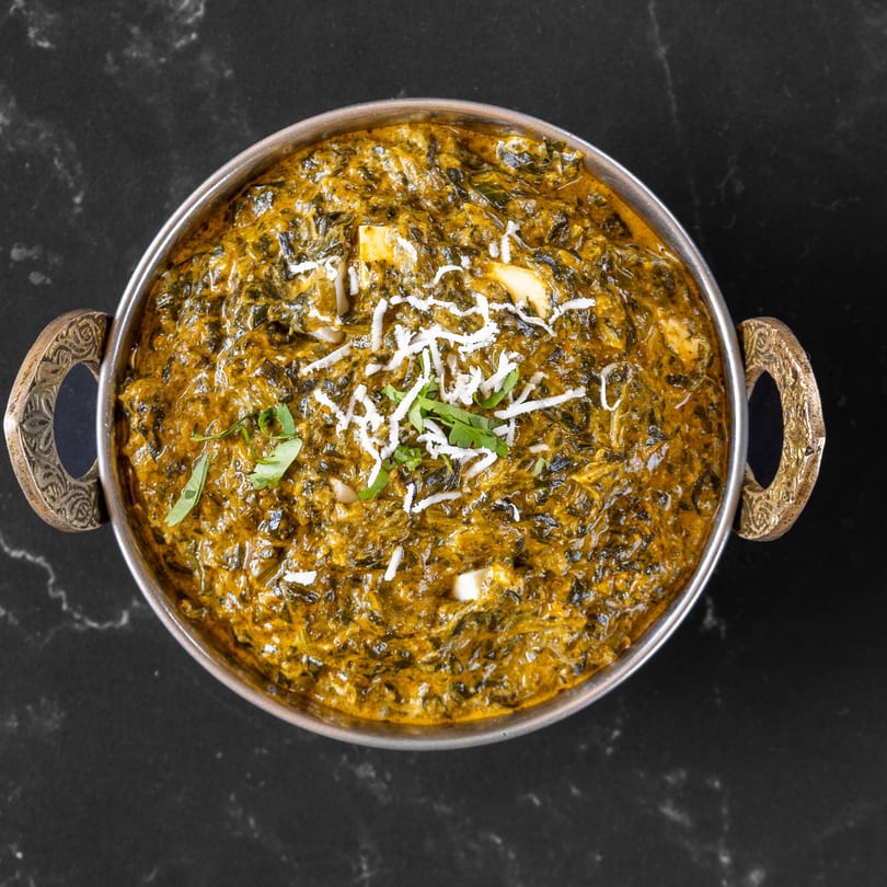 Palak Paneer, a vibrant green Indian spinach and cheese curry, garnished with fresh cilantro and shredded cheese.