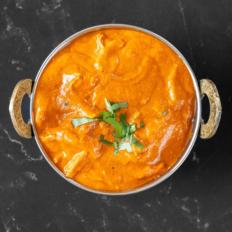 Overhead view of a metal bowl filled with orange Indian curry, garnished with fresh cilantro.