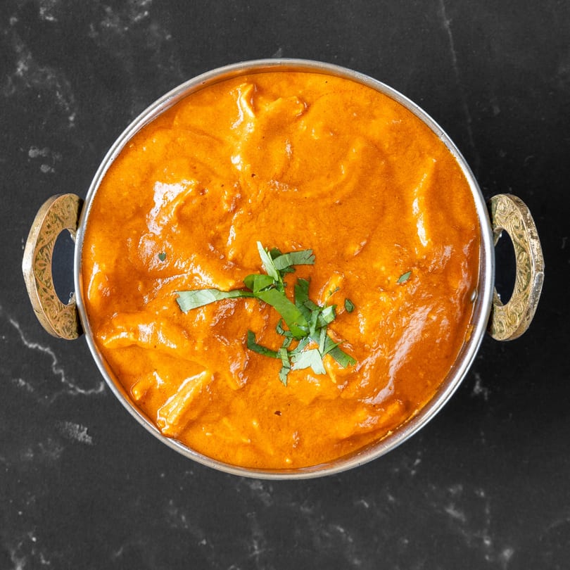 Overhead view of a metal bowl filled with orange Indian curry, garnished with fresh cilantro.